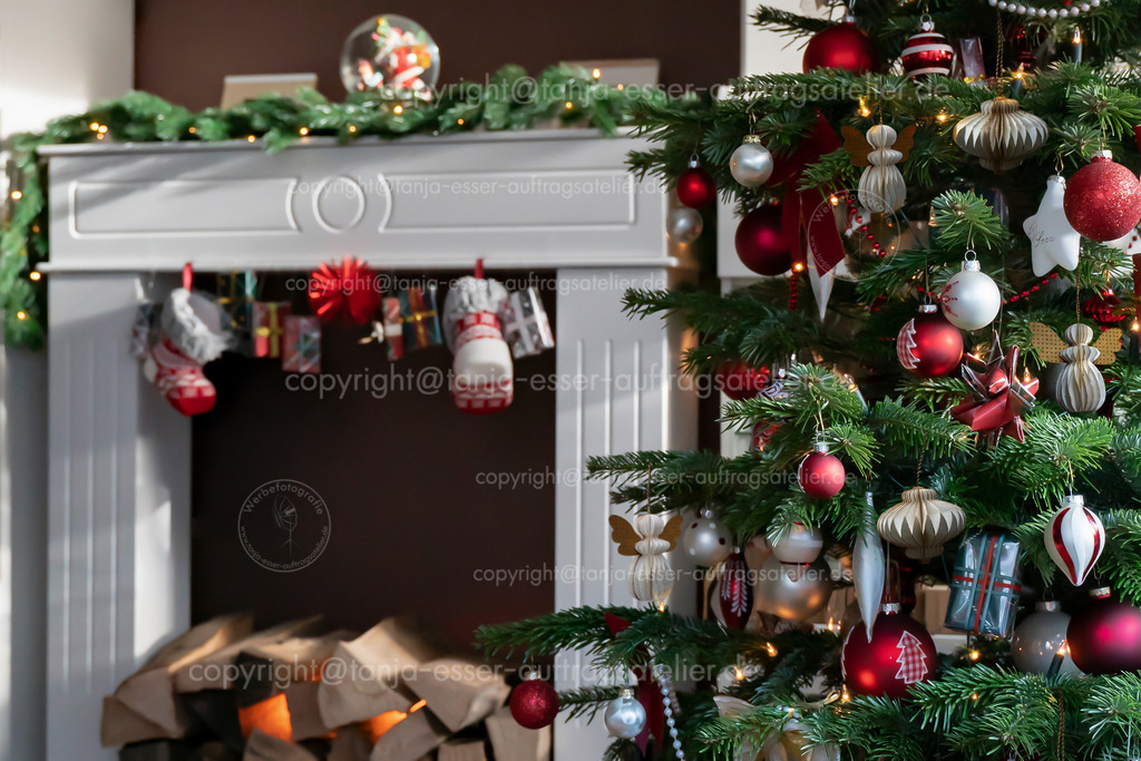 Weihnachtsbaum im Wohnzimmer Wabenanhaenger D | Geschmückter Weihnachtsbaum, echte Nordmanntanne vor unscharfem Wohnzimmermöbel. Makrofotografie zeigt Weihnachtsbaum Ornamente aus Waben Papier und Kugeln in Rot, Weiß und Champagner.