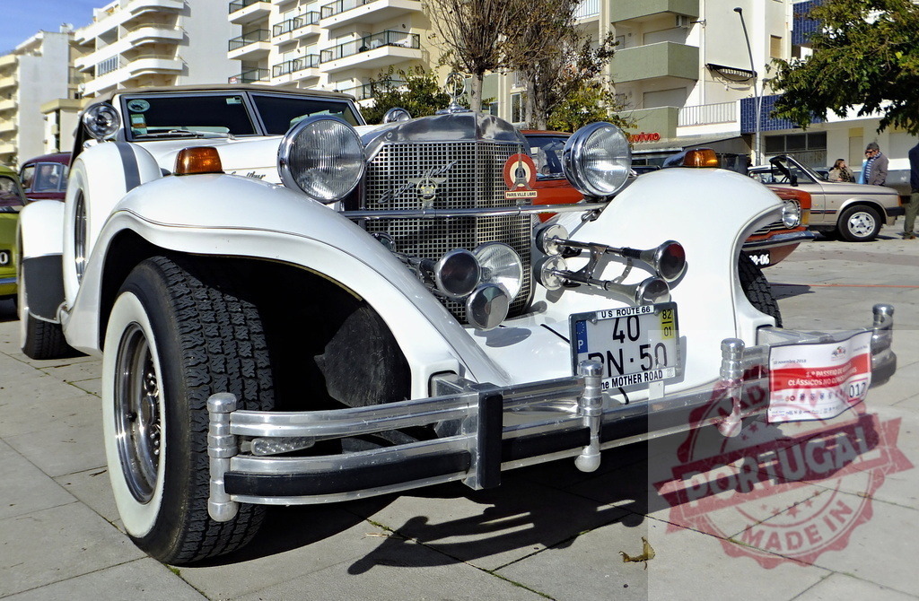 Excalibur Phaeton Series IV parked in urban environment displaying its classic design | White Excalibur Phaeton Series IV classic car parked on a paved street in an urban setting, showcasing its vintage elegance - Realisiert mit Pictrs.com