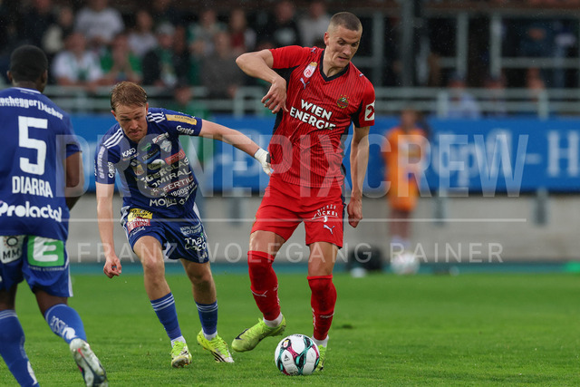 TSV Egger Glas Hartberg vs SK Rapid Wien – Championship Group    | Hartberg, Austria, 19.Apr.26 - SOCCER - ADMIRAL Bundesliga, TSV Egger Glas Hartberg vs SK Rapid Wien. The image shows Benjamin Markus (Hartberg) and Nenad Cvetkovic (SK Rapid Wien) in rain. 