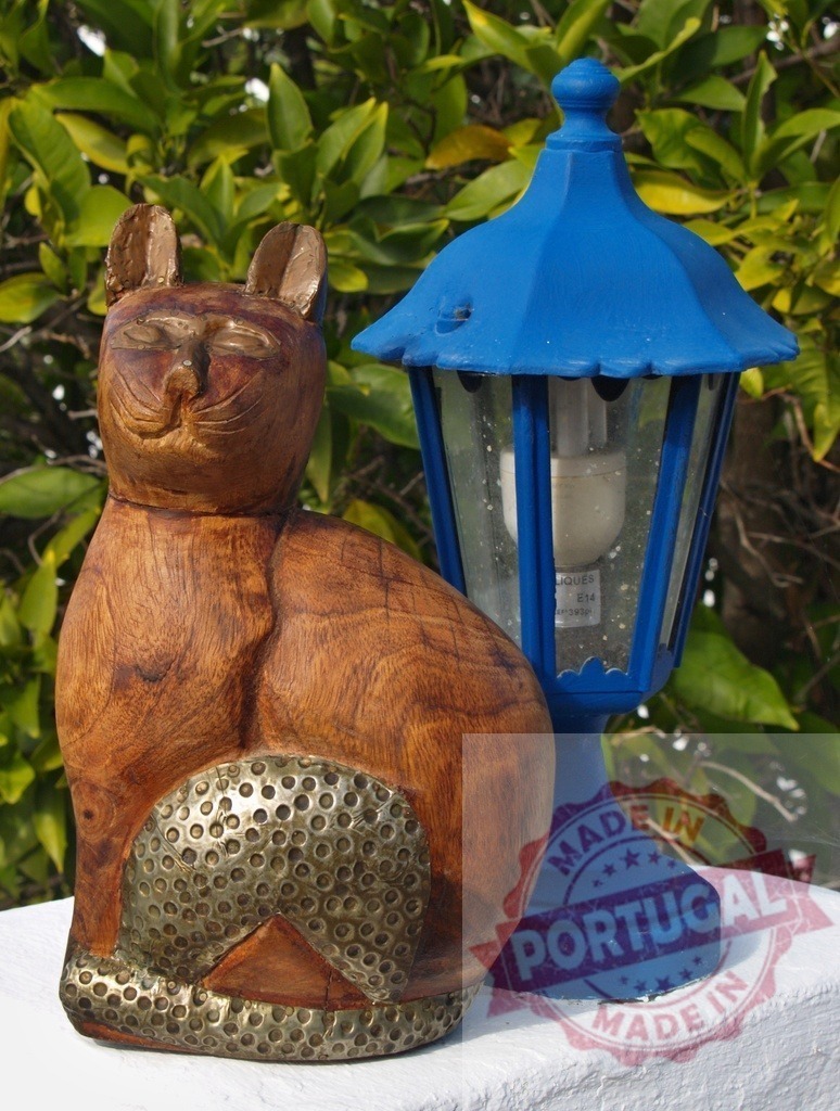 Wooden cat figurine with blue garden lantern | Wooden cat statue with brass detail sitting next to a blue outdoor lantern on a white wall - Realized with Pictrs.com