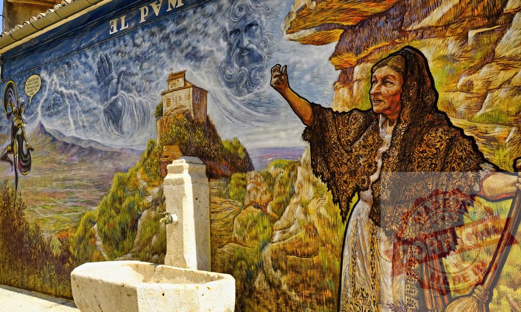 Street art mural depicting an old woman and landscape | Colorful building wall mural showing traditional Spanish culture and a stone fountain - Realisiert mit Pictrs.com