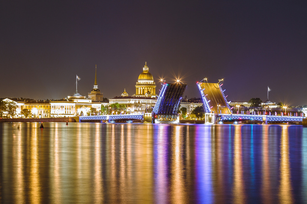 Palastbrücke bei Nacht – Sankt Petersburg | Die geöffnete Palast-Brücke über der Newa vor der nächtlich beleuchteten Kulisse von Sankt Petersburg.Die leuchtenden Brückenflügel, historische Architektur und die ruhigen Spiegelungen auf dem Wasser verbinden sich zu einer monumentalen Schwarz-Weiß-Komposition. Die Langzeitwirkung des Wassers verstärkt die Ruhe der Szene und bildet einen starken Kontrast zur markanten Konstruktion der geöffneten Brücke.Ein atmosphärisches Fine-Art-Motiv über Architektur, Licht und die besondere nächtliche Silhouette Sankt Petersburgs. - Realisiert mit Pictrs.com
