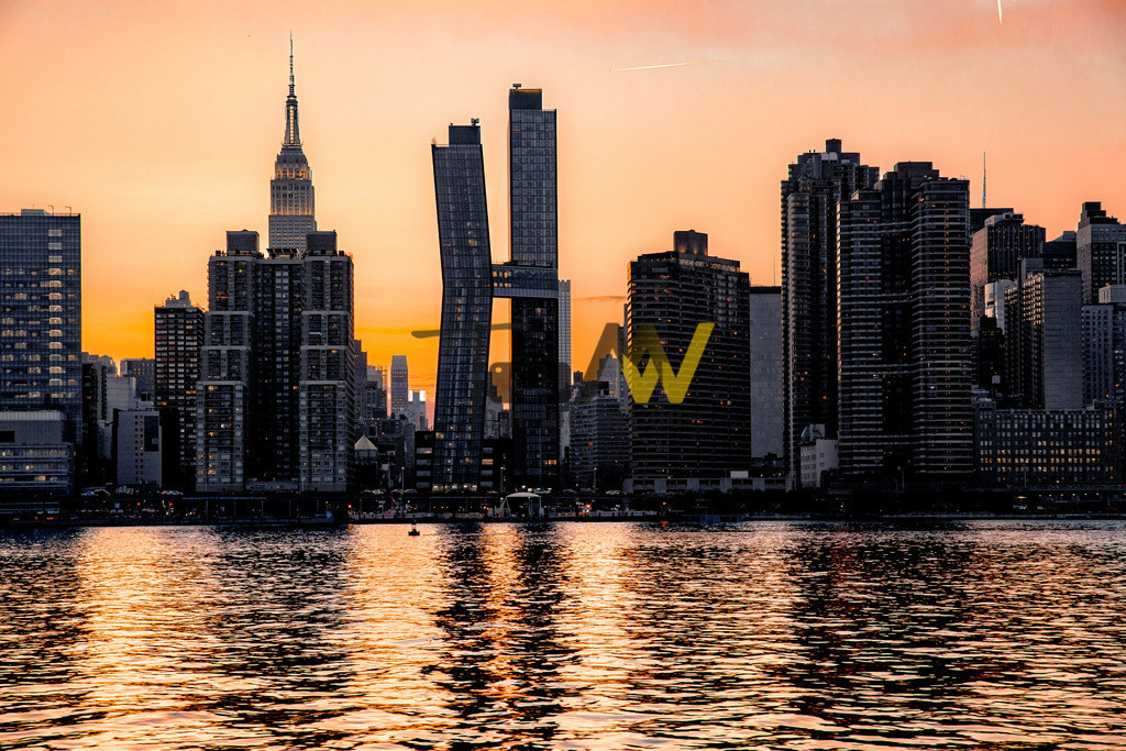 Skyline von New York bei einem tollen Sonnenuntergang--USA | Das Bild zeigt die Skyline von New York City bei Sonnenuntergang, aufgenommen von der anderen Seite des Hudson River in New Jersey oder eventuell vom East River in Queens. Der Anblick bietet eine Panoramaaussicht auf die markanten Wolkenkratzer Manhattans, einschließlich des Empire State Buildings, das im goldenen Abendlicht erstrahlt. Details zur AnsichtStandort: Die Perspektive lässt auf einen Standort in Weehawken, New Jersey, schließen, möglicherweise in der Nähe des Sheraton Lincoln Harbor Hotels, das für diesen Blick bekannt ist.Atmosphäre: Der Sonnenuntergang taucht die Szene in warme Farben, die sich im Wasser des Flusses spiegeln.Gebäude: Neben dem berühmten Empire State Building sind weitere moderne Gebäude zu erkennen. Der goldene Schein des Sonnenuntergangs ist ein beliebtes Motiv für Fotografen.  - Realisiert mit Pictrs.com