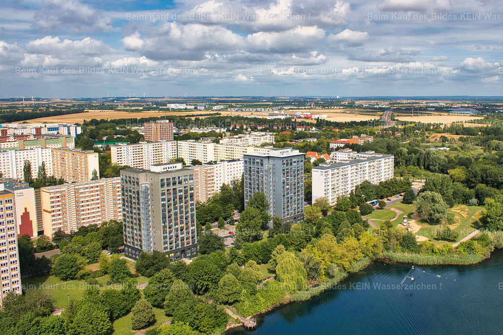 Magdeburg-Neustädter-See-Hochhaus-Schrotebogen_4360 | Blick auf die Hochhäuser am Schrotebogen im Norden Magdeburgs. Sie sind Teil der großflächigen Wohnbebauung, die in der DDR entstand, um den enormen Wohnungsbedarf der wachsenden Stadt zu decken.Im Magdeburger Norden wurden ab den 1970er Jahren ganze Wohngebiete mit industriell gefertigten Plattenbauten errichtet. Zehn- und sechsgeschossige Wohnblöcke sowie einzelne 16-geschossige Wohnhochhäuser prägten die neue Stadtlandschaft. Der Wohnungsbau folgte dabei einem streng geplanten System aus wenigen standardisierten Gebäudetypen, die in großer Zahl errichtet werden konnten.Auch am Schrotebogen ist dieser Wandel bis heute ablesbar. Was damals als moderner und dringend benötigter Wohnraum entstand, gehört heute zur Geschichte des Magdeburger Nordens. Einige der Gebäude wurden inzwischen saniert, andere verschwanden im Zuge des späteren Stadtumbaus.Das Luftbild zeigt damit ein Stück Magdeburger Alltagsgeschichte aus der Zeit des großen DDR-Wohnungsbaus. - Realisiert mit Pictrs.com
