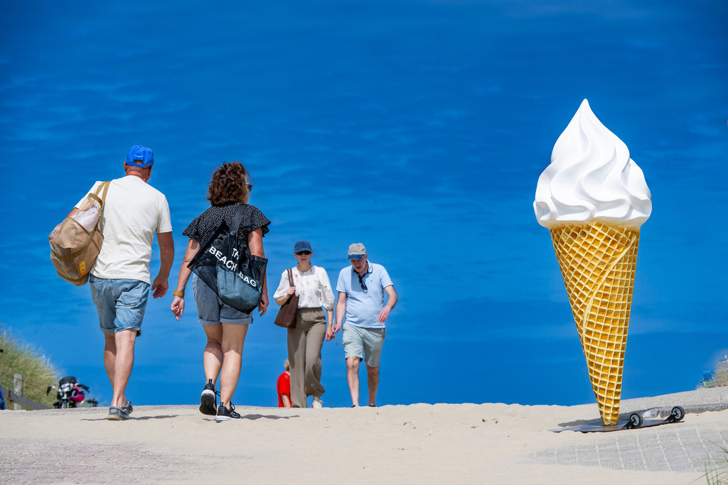 Sommerliche Leichtigkeit auf Texel | Ein Hauch von purer Urlaubsfreude auf der Nordseeinsel Texel: Unter einem strahlend blauen Sommerhimmel spazieren Urlauber entspannt über den Dünenweg in Richtung Strand. Eine übergroße Softeis-Skulptur am Wegesrand setzt einen verspielten Blickfang und weckt sofort Erinnerungen an sonnige Ferientage, süße Erfrischungen und das unbeschwerte Gefühl von Sommer am Meer. Das kräftige Blau des Himmels und der helle Sand schaffen eine lebendige, fröhliche Atmosphäre, die Lust auf Sonne, Strand und Inselleben macht. - Realisiert mit Pictrs.com