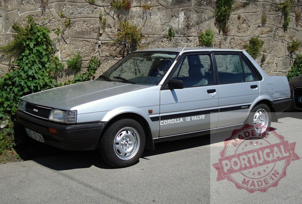 Silver Toyota Corolla 12 Valve parked near a stone wall | Classic silver Toyota Corolla 12 Valve parked on the street next to a stone wall with some vegetation - Realisiert mit Pictrs.com