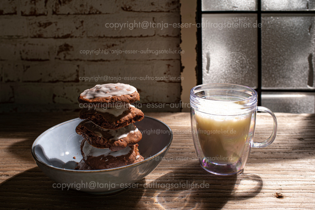 Berliner Brot Santa Claus D | Plätzchen aus Lebkuchenteig stehen gestapelt in einer Schale. Ein Glas Milch steht daneben vor einem vereisten Fenster. Es ist Abend und der Mond leuchtet durch das Fenster. Gaben für Santa Claus. 