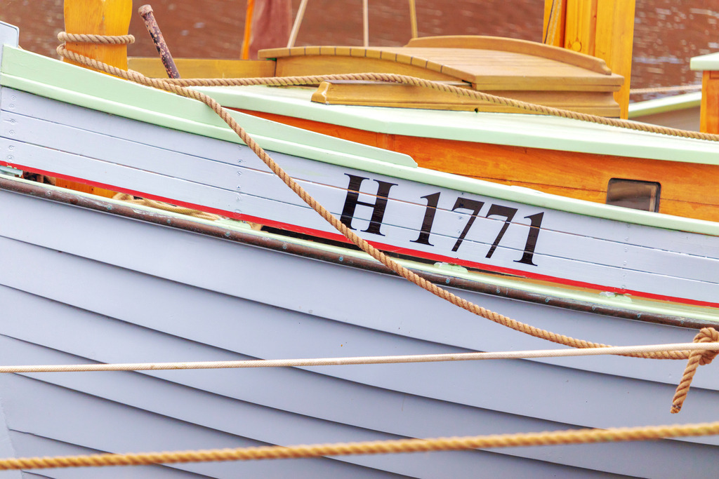 Wandbild: Boot im Hafen | Dieses Wandbild im Querformat zeigt ein Boot im Ostseehafen. Im Vordergrund hängen Seile. - Realisiert mit Pictrs.com