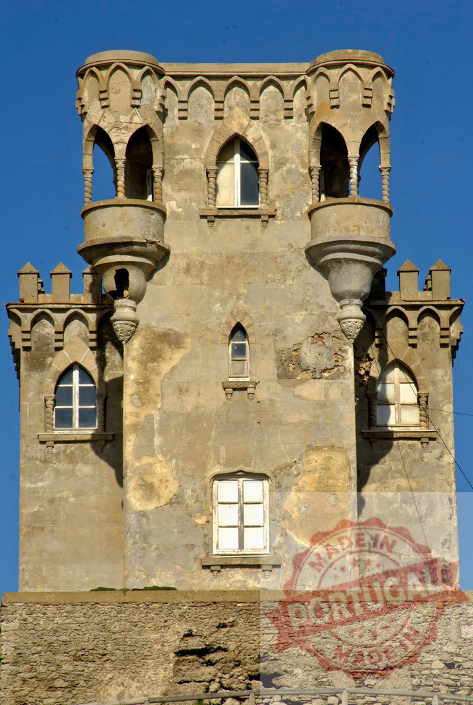 Historic castle tower with balconies and gothic windows. Espana - Cadiz | Ancient castle tower standing against a clear blue sky, showing aged stone and intricate details - Realized with Pictrs.com