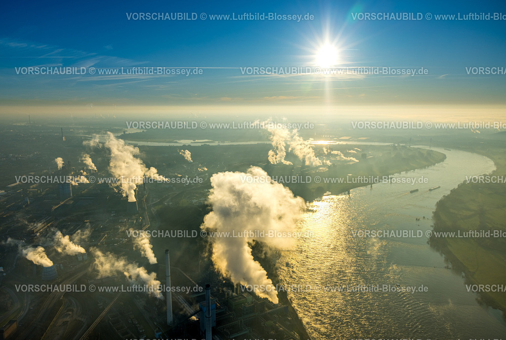 Duisburg241202921 | Luftbild, Thyssen Krupp Steel Europe AG am Fluss Rhein, Werkshafen Schwelgern, Gegenlicht und strahlenförmige Sonne am blauen Himmel, qualmende rauchende Schornsteine, Marxloh, Duisburg, Ruhrgebiet, Nordrhein-Westfalen, Deutschland
