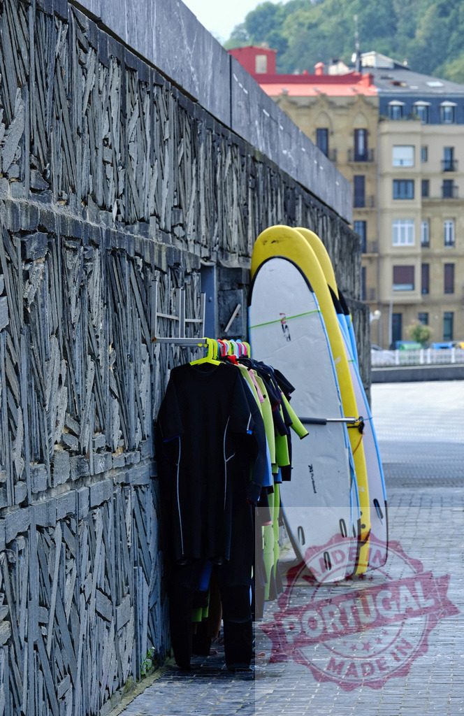 Surfboards and wetsuits drying by wall in San Sebastian | Surfboards and wetsuits hanging to dry at a surf school near the water - Realized with Pictrs.com