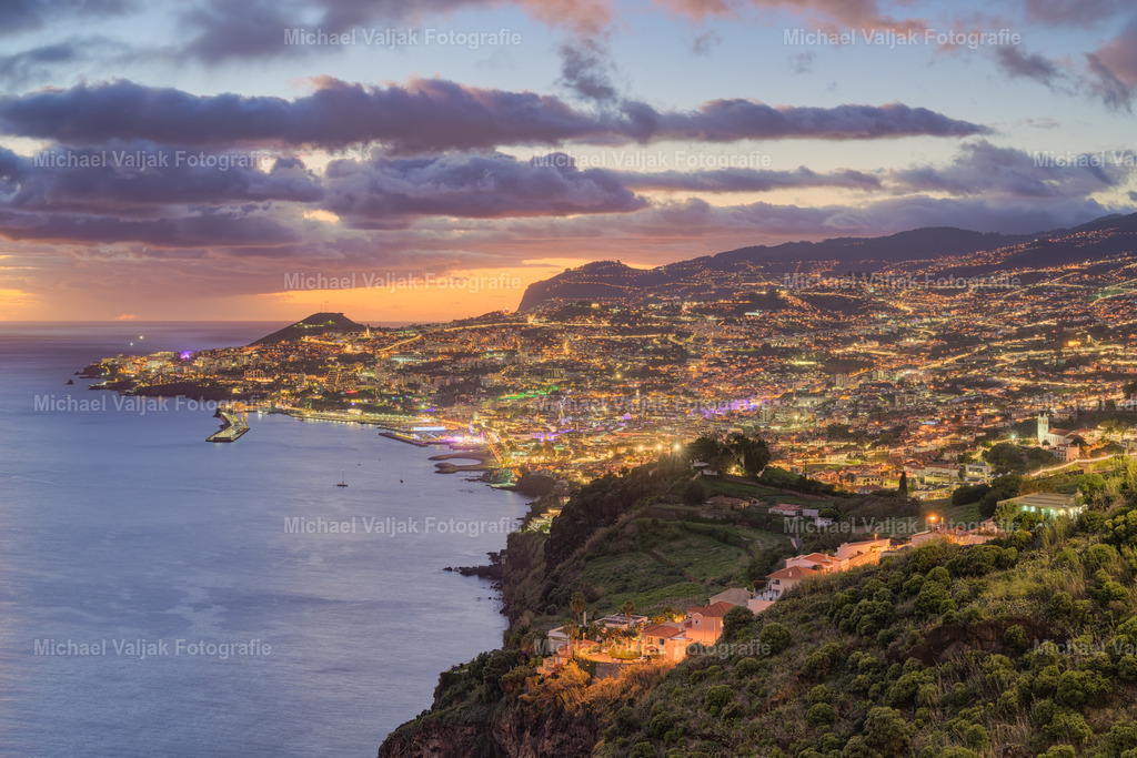 Blick auf Funchal am Abend | Der Miradouro do Pináculo bietet einen atemberaubenden Blick über die beleuchtete Stadt Funchal am Abend. Die funkelnden Lichter der Stadt erstrecken sich bis zum Horizont und schaffen eine magische Atmosphäre. Die Kombination aus den Lichtern der Stadt und dem sanften Glühen des Himmels macht diesen Aussichtspunkt zu einem besonderen Erlebnis.Dieser Ort ist perfekt, um die Schönheit von Funchal bei Nacht zu genießen und die friedliche Stimmung zu erleben. Ein Besuch hier ist ein Muss für alle, die die Insel Madeira erkunden und unvergessliche Momente festhalten möchten. - Realisiert mit Pictrs.com