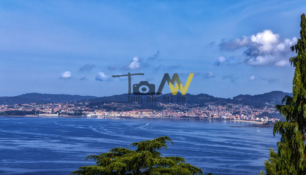 Vigo mit bewohntem Küstenstreifen direkt am Meer,blauer Himmel | Die Ansicht zeigt die Küste von Vigo, Spanien, aufgenommen von Canido aus. Vigo ist eine Hafenstadt in der Region Galicien im Nordwesten Spaniens.Die Stadt liegt an der Ría de Vigo, einer der tiefsten Rías Baixas.Die Gegend ist bekannt für ihre Strände und Meeresfrüchte. - Realisiert mit Pictrs.com