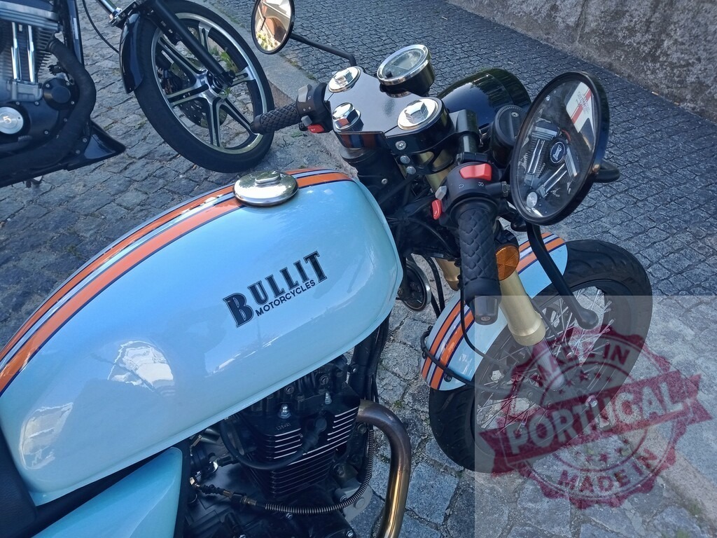 Bullit Motorcycle Parked on Cobblestone Street | Close-up of a light blue and orange Bullit motorcycle parked on a cobblestone street, showcasing its classic design - Realized with Pictrs.com