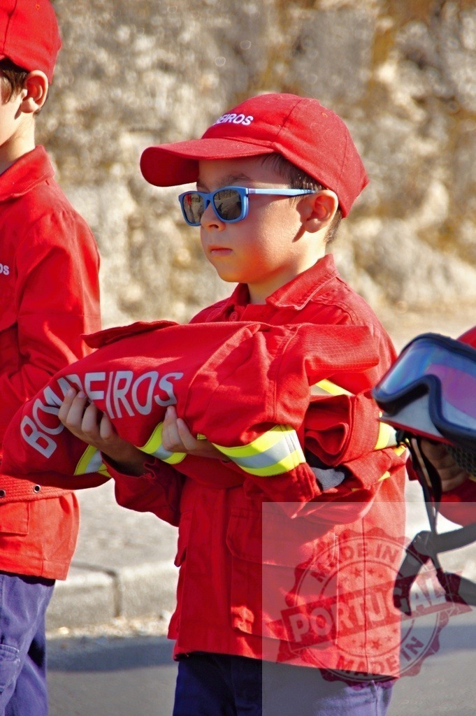 Young firefighter carrying folded uniform during a ceremony | Procession 15.08.2025 - Assumption Day - Paco de Sousa, Portugal Child wearing firefighter uniform and sunglasses carrying a folded uniform during a ceremony - Realisiert mit Pictrs.com