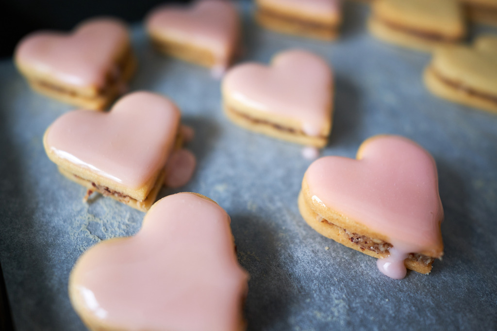 mit Nussmasse gefüllte Herzkekse und rosa Glasur | Austria - July 12, 2022: mit Nussmasse gefüllte Herzkekse auf einem Backblech mit rosa Zuckerglasur. - Realisiert mit Pictrs.com
