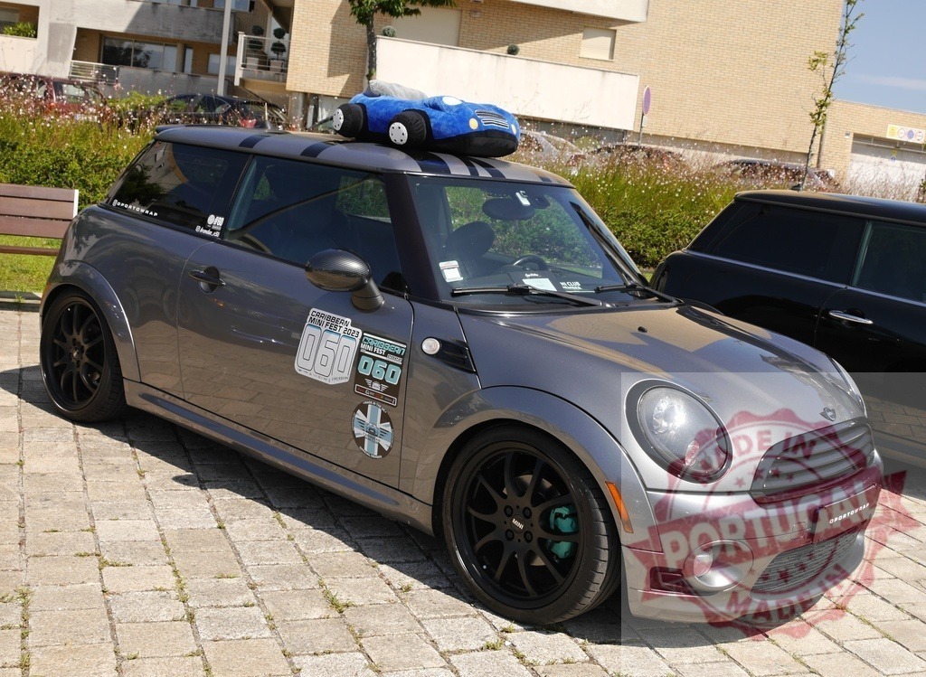 Customized Mini Cooper car parked at a car show | Grey modified Mini Cooper car displaying event stickers and a plush toy on roof - Realized with Pictrs.com