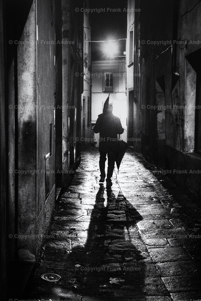 Nach dem Regen | Nacht in der Altstadt von Barga in der Toskana. Ein Mann geht allein mit zwei Regenschirmen durch die regennasse Altstadt. Straßenfotografie aus Italien in schwarz und weiß. - Realisiert mit Pictrs.com