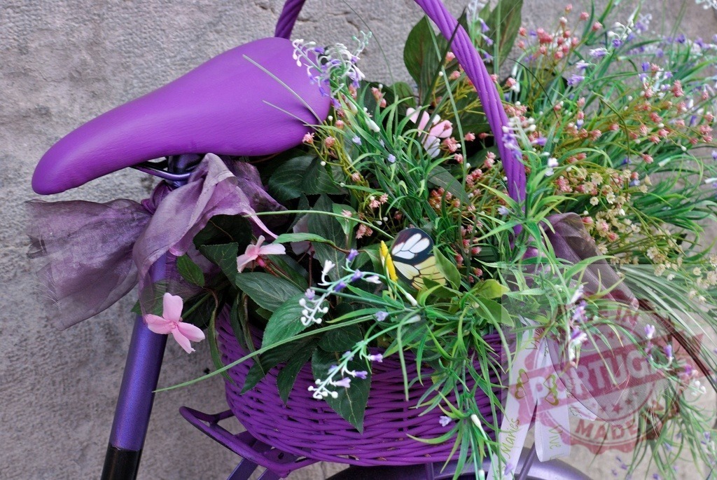 Purple bicycle with basket of spring flowers and butterfly | Purple decorative bicycle holding a woven basket filled with spring flowers and a butterfly - Realized with Pictrs.com
