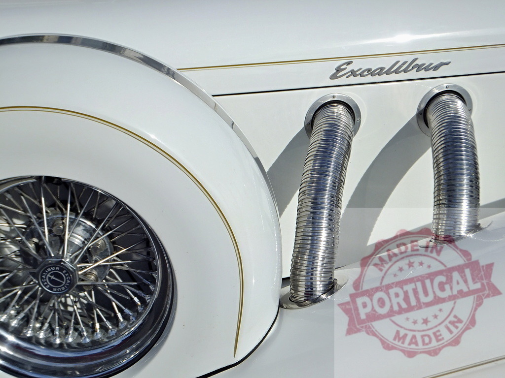 Close-up of an Excalibur automobile showing exhaust pipes and wheel | White Excalibur classic car detail featuring exhaust pipes and front wheel - Realized with Pictrs.com