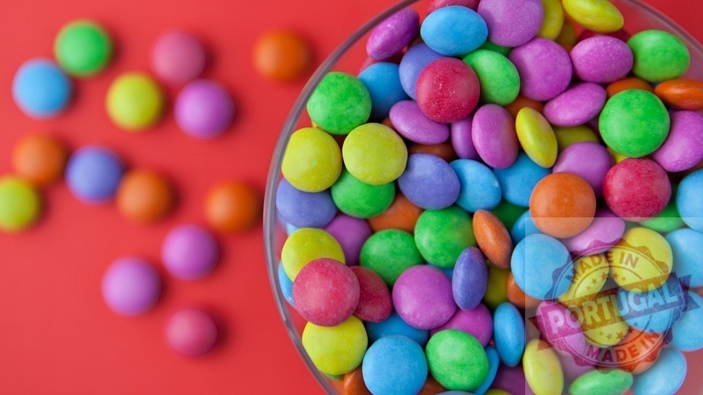 Colorful candy coated chocolate buttons spilling from a glass | Bright sugar-coated sweets filling a bowl and scattered on a red background - Realisiert mit Pictrs.com