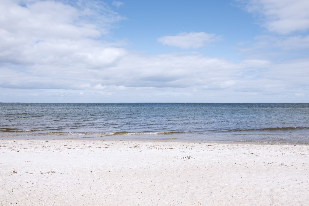 Wandbild: Meeresstille Falshöft - Weitblick am Ostseestrand | Dieses minimalistische Wandbild fängt die friedvolle Weite der Ostseeküste in Falshöft in vollkommener Klarheit ein. Der helle, feine Sandstrand im Vordergrund führt direkt zum ruhigen Meer, während sich darüber ein malerischer Wolkenhimmel bis zum fernen Horizont spannt. Die dezenten Blautöne und die ausgewogene Komposition vermitteln eine tiefe, meditative Ruhe – eine stilvolle Bereicherung für anspruchsvolle, moderne Interieurs mit einem Gespür für zeitlose Ästhetik.