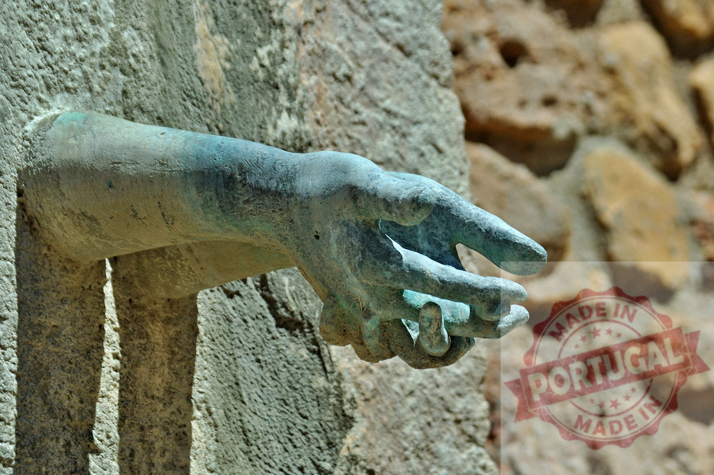 Bronze sculpture hand reaching out from stone wall | Bronze sculpture of a human hand emerging from a rough stone wall, showing green patina - Realized with Pictrs.com