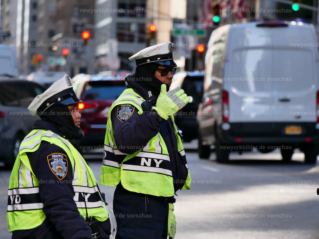 New Yorker Polizisten in Midtown | Mitten in Midtown Manhattan, wo das Leben in einem unaufhörlichen Rhythmus pulsiert, stehen New York City Polizisten und regeln den Verkehr auf einer der meistbefahrenen Straßen der Metropole. Es ist ein klarer, sonniger Wintertag, die Luft ist eiskalt und frisch, während die Sonne die Fassaden der Wolkenkratzer in goldenes Licht taucht. Autos drängen sich Stoßstange an Stoßstange, gelbe Taxis schlängeln sich durch die engen Lücken, und Fußgänger eilen über die Kreuzungen, eingehüllt in dicke Mäntel. Die Polizisten sind die Ruhe im Chaos, ihre Gesten präzise und bestimmt, ein sichtbares Symbol für Ordnung in einer Stadt, die niemals stillsteht. Dieses Bild erzählt von der Kraft und Organisation, die hinter dem scheinbaren Durcheinander steckt, und von der einzigartigen Atmosphäre, die Manhattan im Winter ausstrahlt: klar, lebendig, voller Energie. Wer New York liebt, erkennt hier die Essenz der Stadt – ein Ort, an dem selbst die Kälte nicht die Wärme des urbanen Lebens vertreiben kann.