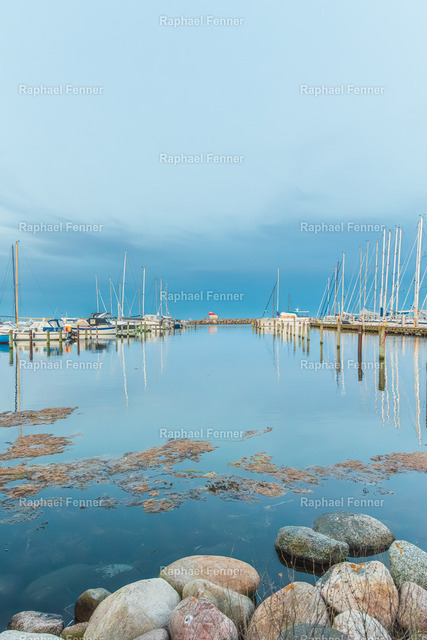 Yachthafen in Dänemark | Spiegelung am Meer | Die ruhige Atmosphäre eines dänischen Yachthafens spiegelt sich nahezu perfekt im stillen Wasser. Die zahlreichen Segelmasten, der kleine Leuchtturm am Ende des Stegs und die sanften Blautöne verleihen diesem Motiv eine besondere Gelassenheit. Entstanden an der dänischen Küste, fängt das Bild die maritime Stimmung Skandinaviens auf zeitlose Weise ein.Als hochwertiger Fine-Art-Druck eignet sich dieses Motiv ideal für Wohnräume, Büros oder Ferienhäuser und bringt die Ruhe und Weite der nordischen Küstenlandschaft in jedes Zuhause.