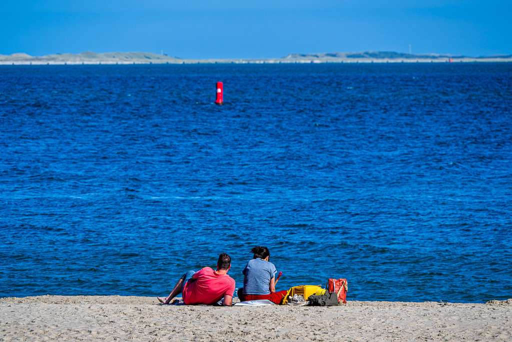 Spätsommerlicher Strandtag auf Texel: Paar genießt Auszeit an der Nordsee | Ein Paar sitzt entspannt im hellen Sand am Strand der holländischen Nordseeinsel Texel und blickt auf das tiefblaue Meer. Die ruhige Küstenatmosphäre fängt Momente von Erholung, Zweisamkeit und Urlaubsidylle ein. Mit leichtem Gepäck am Strand bietet die Szene ein stimmungsvolles Motiv für Themen wie Tourismus, Freizeit, Naherholung und Reisen an die niederländische Küste. - Realisiert mit Pictrs.com