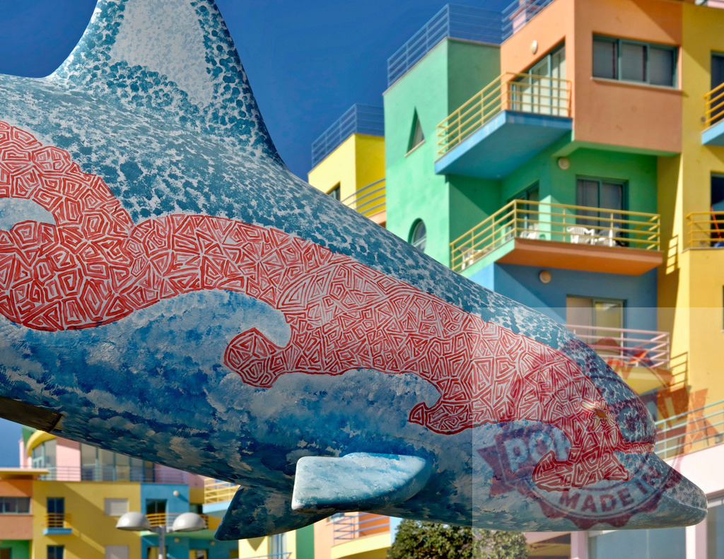 Colorful dolphin sculpture with vibrant urban architecture building | Colorful dolphin sculpture stands against vibrant urban architecture, creating playful contrast - Realized with Pictrs.com