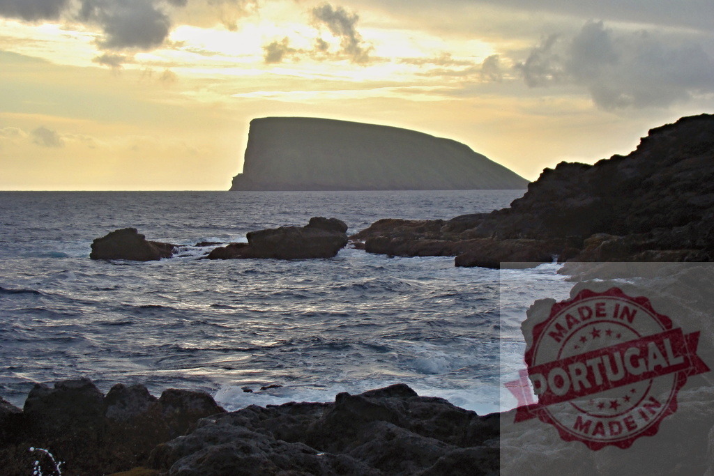 Pico island sunset over rocky São Jorge coast | Ocean waves breaking on dark shore rocks with a distant island silhouette against a golden sky - Realized with Pictrs.com