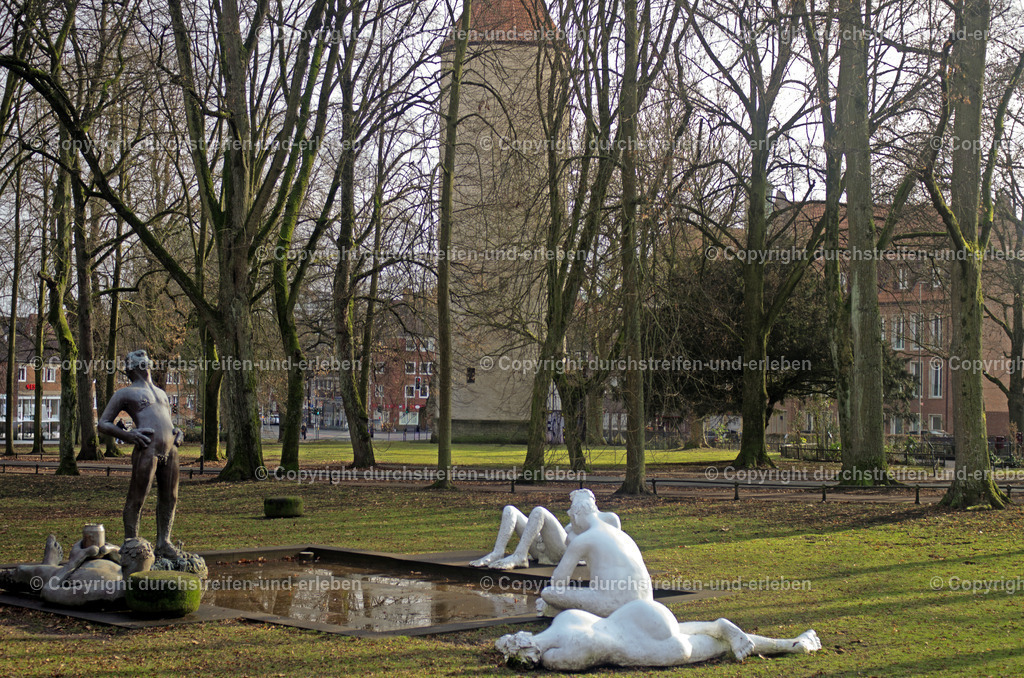 Sketch for a Fountain in Münster | Der als „Eisenman-Brunnen“ bekannte Brunnen in Münster trägt den offiziellen Titel „Sketch for a Fountain“. Er wurde von der amerikanischen Künstlerin Nicole Eisenman für die Skulptur Projekte 2017 geschaffen. Er gilt als bedeutendes Symbol für Toleranz und Vielfalt. Der Brunnen befindet sich an der Promenade, nahe am am Kreuztor.. Dahinter steht der Buddenturm, einst Teil der Stadtbefestigung im Mittelalter.  Fünf übergroße Figuren aus Bronze und Gips umgeben das  Wasserbecken.  - Realisiert mit Pictrs.com
