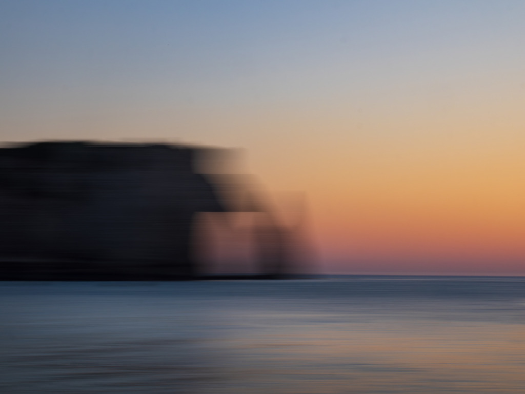 Wächter der Zeit | Étretat  | Wie ein Schatten aus einer fernen Zeit ruht die Felsformation von Étretat am Rand der Bucht. Umhüllt vom goldenen Flüstern der Abenddämmerung, löst sich die Grenze zwischen Materie und Licht. Der Fels erscheint wie ein Wächter der Zeit – ein stilles Relikt aus einer anderen Wirklichkeit. Wie ein Tor zu einer anderen Welt. Erneut verschmilzt durch die verwendete Spezial-Technik des Fotografierens, das Sichtbare mit dem Unsichtbaren. - Powered by Pictrs.com
