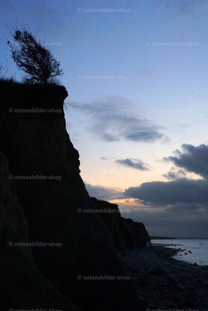 Blaue Stunde an der Steilküste | Eine Wolkenwand schiebt sich vor die Abendsonne und verfinstert den Tag am Meer. Wie im Scherenschnitt erscheinen die Konturen der dunklen Steilküste.