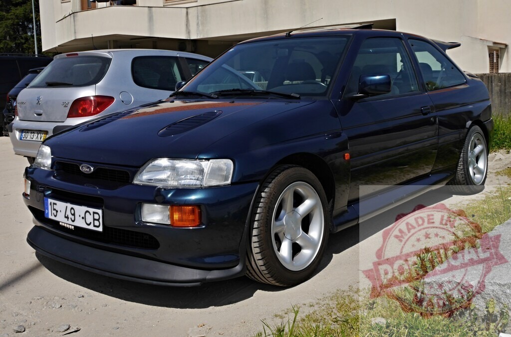 Ford Escort RS Cosworth blue sport classic car parked | Blue Ford Escort RS Cosworth coupe parked on an unpaved surface outdoors - Realized with Pictrs.com