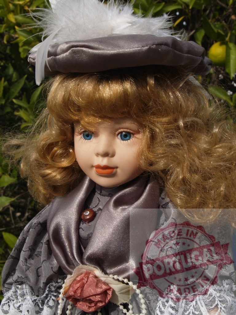 Porcelain doll with blonde hair and blue eyes | Porcelain doll wearing a vintage Victorian dress, hat with feather, and beads - Realized with Pictrs.com
