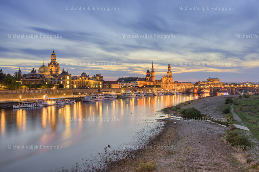 Dresden am Abend | Blick von der Carolabrücke über das Königsufer und die Elbe auf die beleuchtete Skyline von Dresden, mit der Frauenkirche und der Brühlschen Terrasse, dem Residenzschloss und der Katholischen Hofkirche (Kathedrale Sanctissimae Trinitatis) sowie der Semperoper (von links nach rechts). - Realisiert mit Pictrs.com
