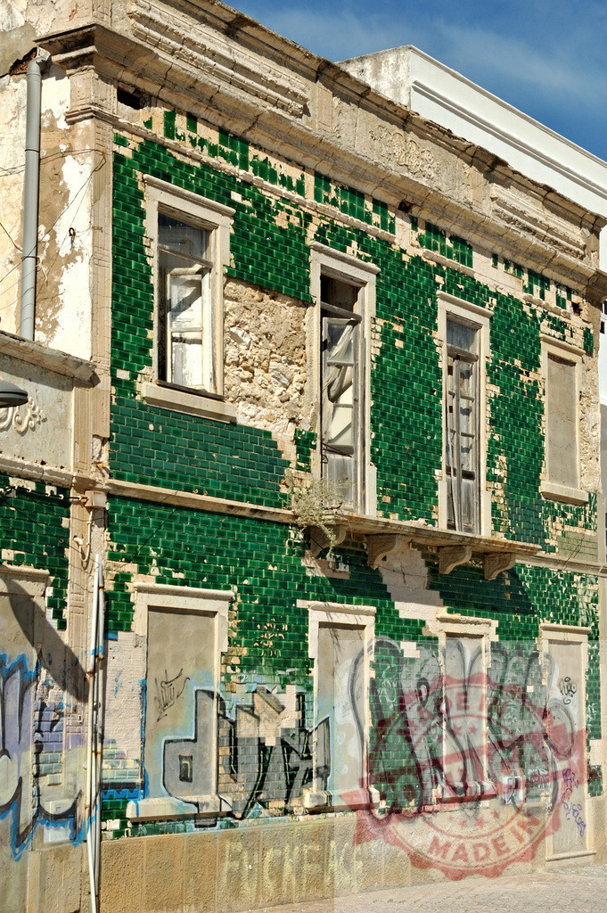 Abandoned building with crumbling green azulejo tiles and graffiti | Abandoned building displaying decaying green azulejo tiles and urban graffiti under a clear sky - Realisiert mit Pictrs.com