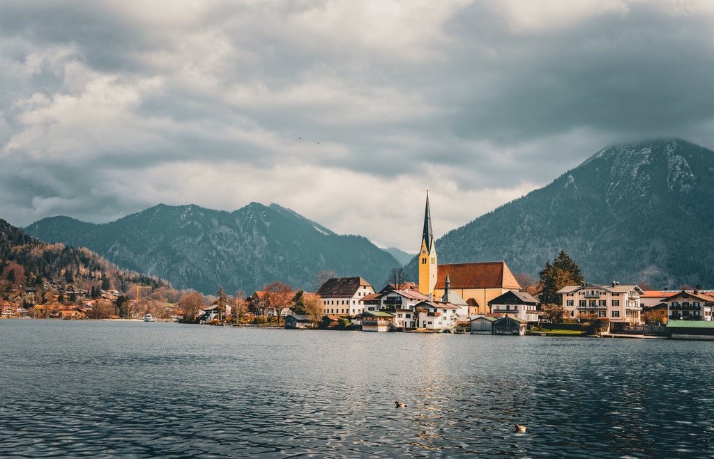 Herbstlicher Blick auf St.Laurentius in Rottach-Egern am Tegernsee,Malerwinkel | Blick über den Tegernsee auf die Ortschaft Rottach-Egern mit der schönen Kirche St. Laurentius. Im Hintergrund thront der Wallberg.Die Abbildung zeigt den Tegernsee in Bayern, Deutschland, mit Blick auf die Stadt Tegernsee und Rottach-Egern. Der Tegernsee liegt etwa 50 Kilometer südlich von München in den Bayerischen Voralpen. Er gilt als einer der saubersten Seen Deutschlands und ist ein beliebtes ganzjähriges Ziel für Aktivurlauber und Erholungssuchende. Die Stadt Tegernsee liegt am Ostufer, während sich Rottach-Egern am Südufer befindet, umgeben von Bergen wie dem Wallberg. Die Region ist bekannt für ihre malerische Landschaft, das anerkannte Heilklima und vielfältige Freizeitangebote. - Realisiert mit Pictrs.com