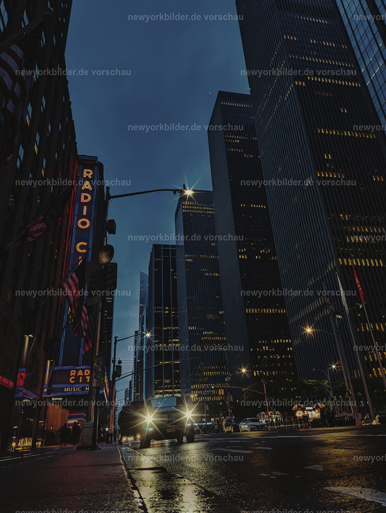 Abend in Midtown Manhattan: regennasse Straßen spiegeln die Lichter, die Radio City Music Hall leuchtet, und die Autos ziehen Lichtspuren – eine Perspektive voller Dynamik. | Ein Abend in Midtown Manhattan, an dem der Regen die Straßen in spiegelnde Flächen verwandelt. Vom Bordstein aus eröffnet sich eine Perspektive voller Bewegung und Licht: Links leuchtet die ikonische Radio City Music Hall in kräftigen Farben, während vor mir die Autos ihre Lichtspuren durch die nassen Straßen ziehen. Die Reflexionen auf dem Asphalt verstärken die Intensität der Szene, und die urbane Kulisse wirkt wie ein lebendiges Gemälde. Es ist ein Moment, der die Energie und den Rhythmus New Yorks einfängt – dynamisch, kontrastreich und voller Atmosphäre.