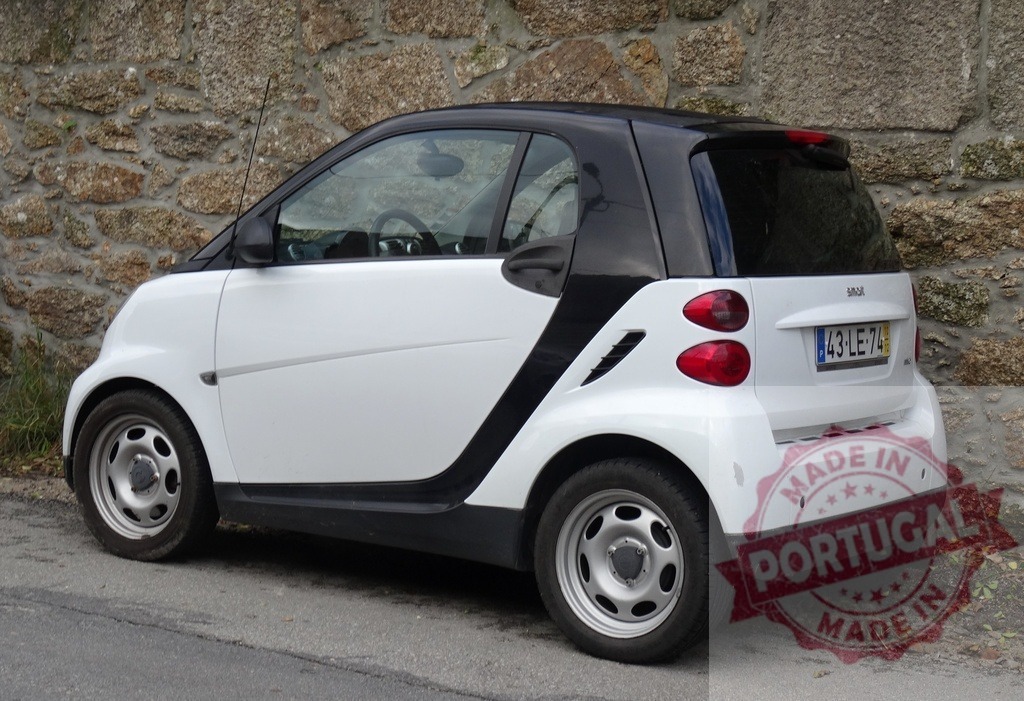 Smart car parked on city street by stone wall | Smart car, white and black, parked on an urban street near a textured stone wall - Realized with Pictrs.com