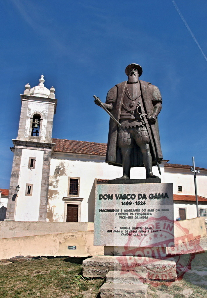 Vasco da Gama statue at church in Vidigueira, Portugal | Vasco da Gama statue standing outdoors against a blue sky with a church in Vidigueira - Realized with Pictrs.com