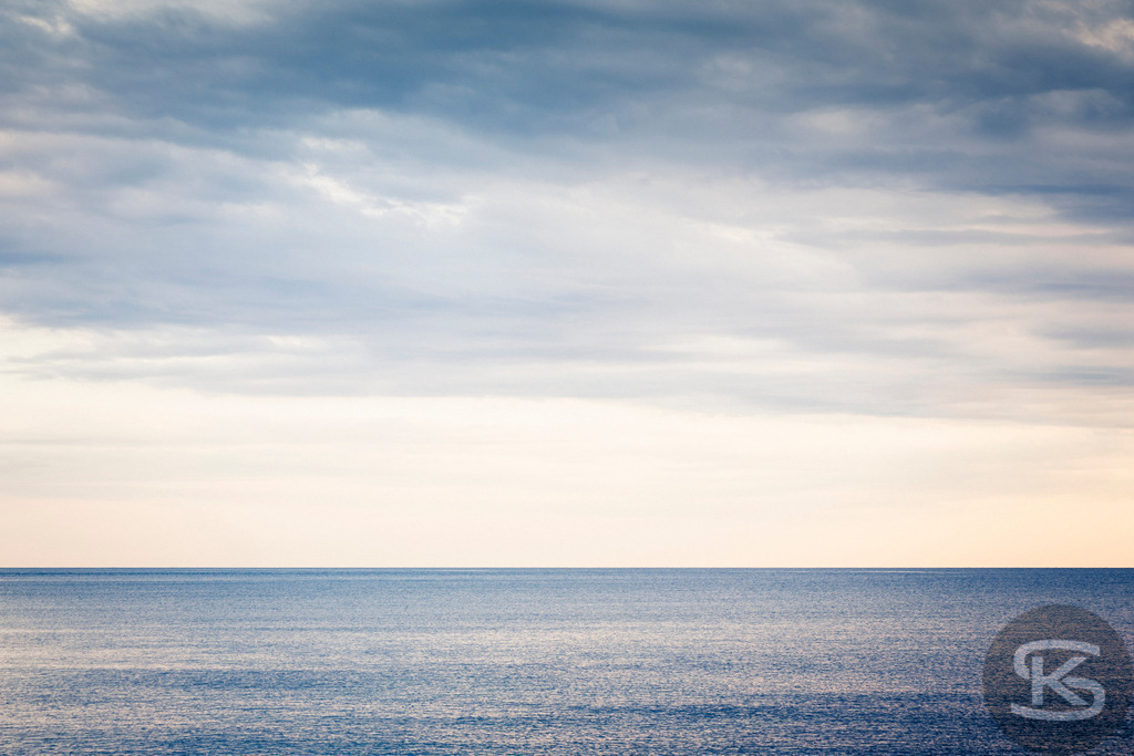 Ruhiger Ozeanhorizont unter pastellfarbenem Himmel | Ein friedliches und minimalistisches Bild einer ruhigen Meereslandschaft bei Tageslicht. Der Horizont erstreckt sich endlos unter einem bewölkten Himmel in zarten Pastellfarben wie Blau, Weiß und hellem Gelb. Das Bild strahlt Ruhe, Stille und Gelassenheit aus. - Realisiert mit Pictrs.com