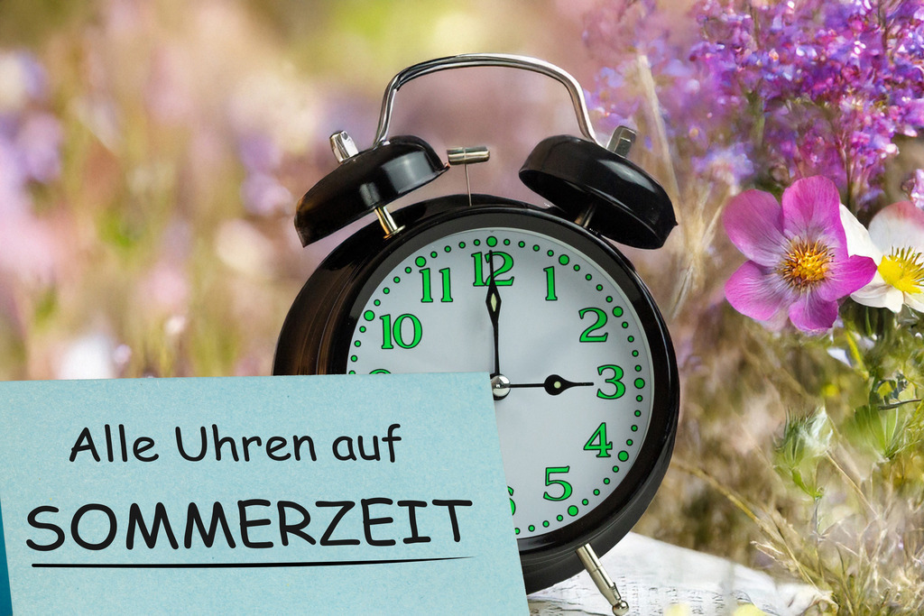 Alle Uhren auf Sommerzeit (Symbolbild Zeitumstellung 2026) | (Fotomontage) Zeitumstellung Sommerzeit Symbolbild: Wecker vor einer Blumenwiese und Text ALLE UHREN AUF SOMMERZEIT - Realisiert mit Pictrs.com