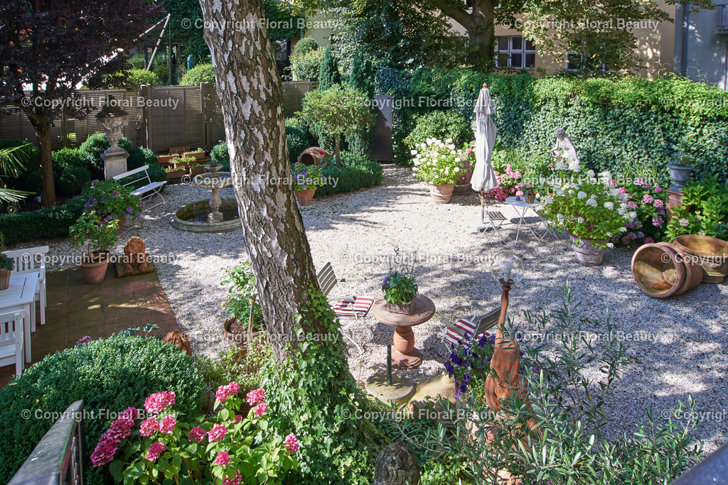 Mediterraner Stadtgarten | Städtischer Garten mit Treppenaufgang zum Balkon. Weiße Gartenmöbel und Tonstatuen und Brunnen. - Realisiert mit Pictrs.com