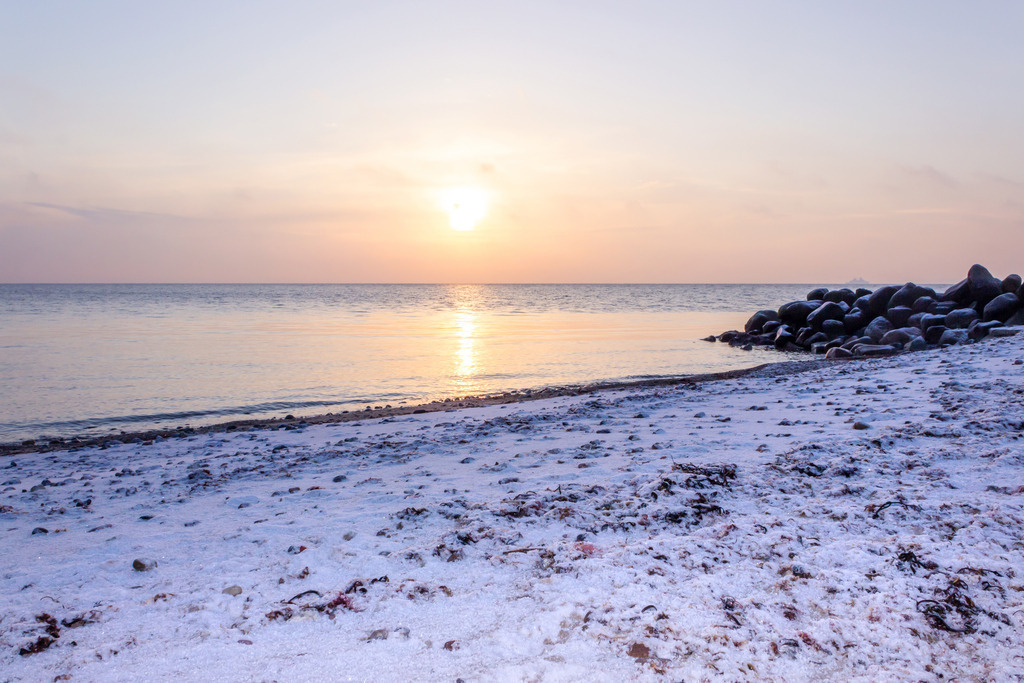 Wandbild: Sonnenaufgang am Ostseestrand | Dieses Wandbild im Querformat zeigt einen schönen Sonnenaufgang am winterlichen Meer. Der Strand im Vordergrund ist leicht verschneit.  - Realisiert mit Pictrs.com