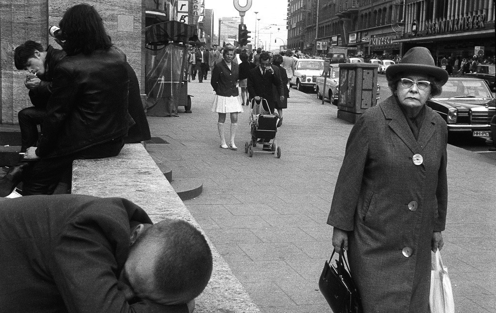011-am-moenckebergbrunnen-hamburg-1971-01 | Eine Passantin wirft einen kritischen Blick auf die Szene mit bietrinkenden Rockern und einem schlafenden jungen Mann. - Realisiert mit Pictrs.com