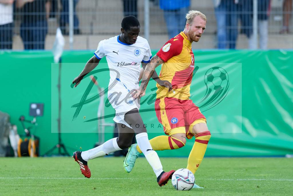 LOTKSC20210809_232 | Fussball, Herren: Philipp Hofmann (Karlsruher SC) und Komlan Fionouke (Sportfreunde Lotte) im Zweikampf beim Spiel der 1. Runde im DFB-Pokal zwischen SF Lotte und Karlsruher SC im Stadion am Lotter Kreuz am 09.08.2021 in Lotte, Deutschland.DFB / DFL REGULATIONS PROHIBIT ANY USE OF PHOTOGRAPHS AS IMAGE SEQUENCES AND/OR QUASI-VIDEO. - Realisiert mit Pictrs.com