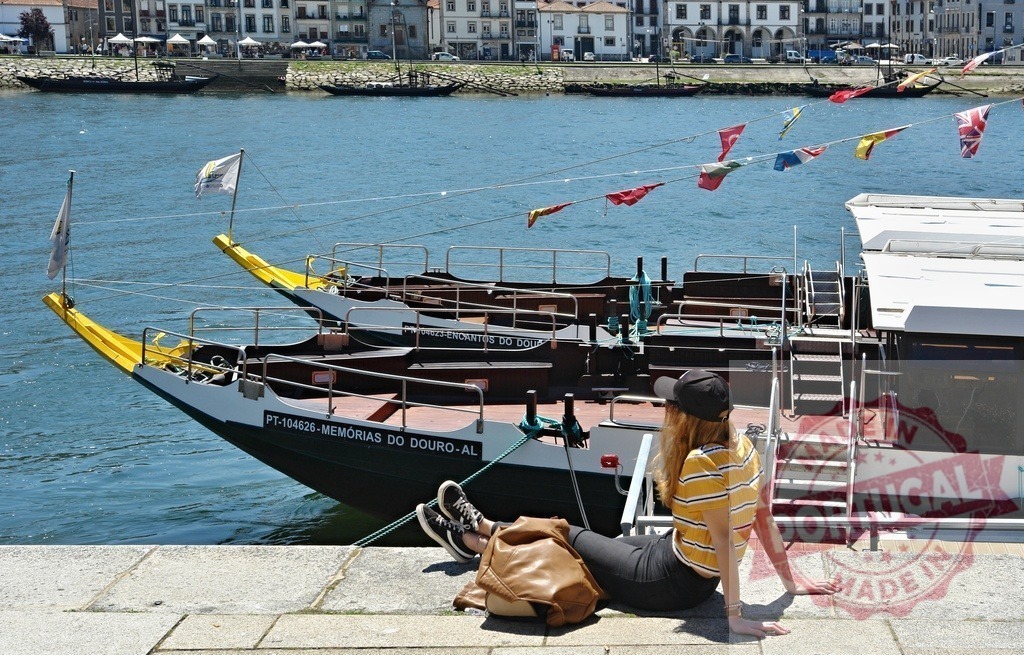 Young woman relaxing on Douro riverfront, Porto Portugal | Young woman sitting on pier watching rabelo boats and river in Porto - Realized with Pictrs.com